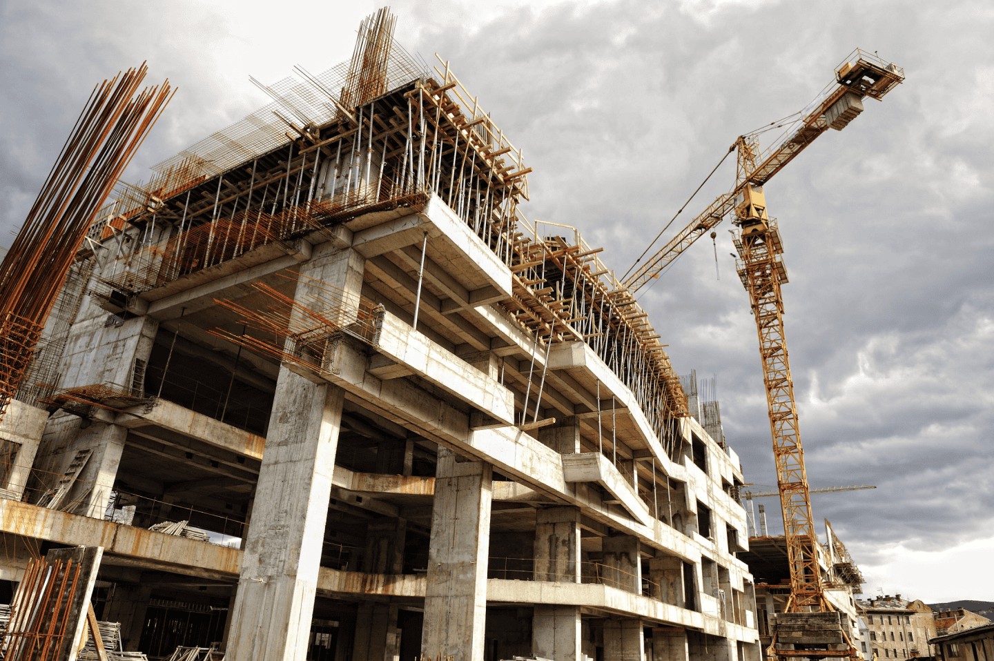 A large concrete building under construction with visible steel reinforcements and a tall crane beside it. A surveyor meticulously examines the site, adding precision to the dramatic scene against an overcast sky.